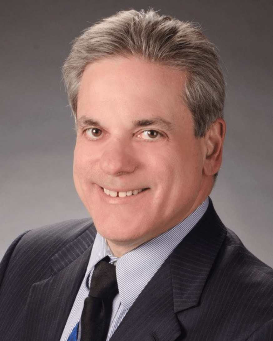 Joe Napoli smiles in a suit jacket and tie while looking at the camera