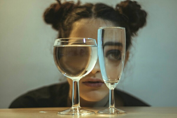 A woman stares at two wine goblets, one empty and one full